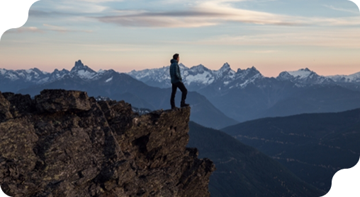 Person standing on a rocky cliff overlooking mountains.